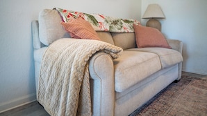 A beige sofa with a patterned throw blanket, a decorative pillow, and a lamp on a side table.