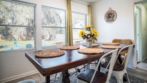 A dining area with a wooden table, four chairs, and a vase with yellow flowers.