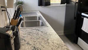 A kitchen with a granite countertop, stainless steel sink, and a black refrigerator.
