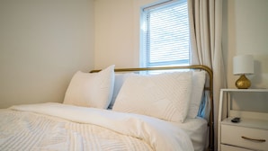 A neatly made bed with a gold frame, white bedding, and a bedside table with a lamp.