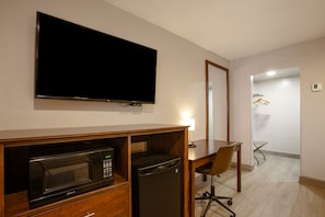 Quarto de hotel com televisão de tela plana, micro-ondas, geladeira, escrivaninha e uma cadeira.