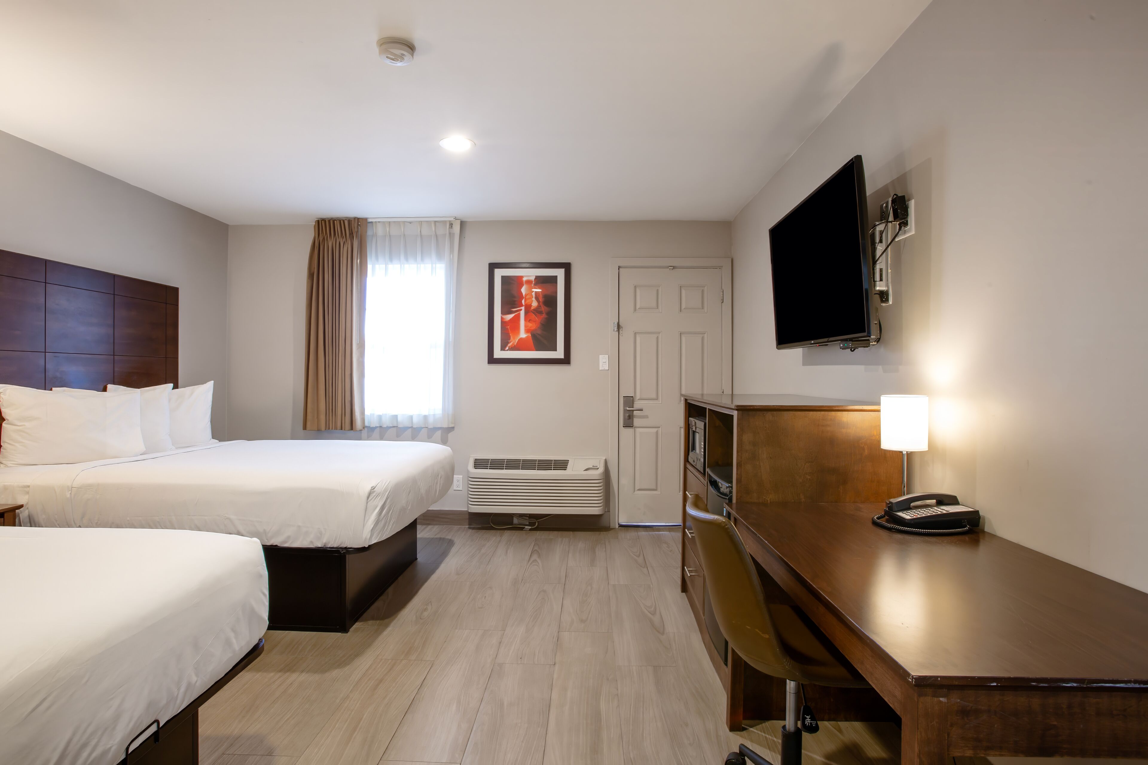 A hotel room with two beds, a desk, a television, a telephone, and an air conditioning unit.