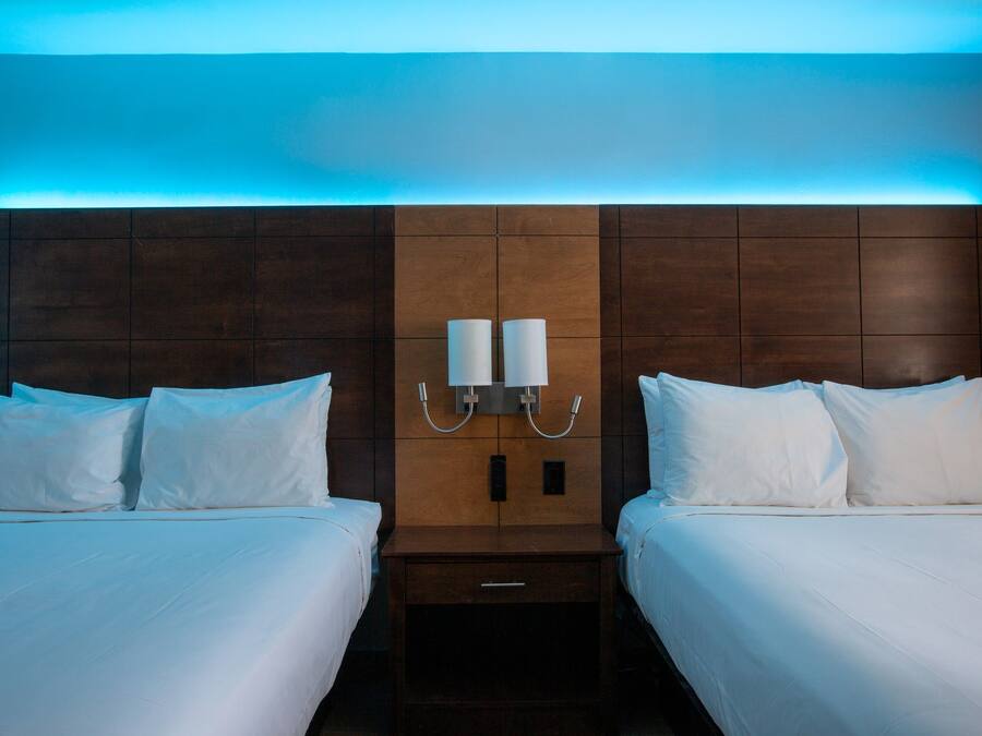 A hotel room with two beds, a wooden headboard, and a nightstand with a lamp.