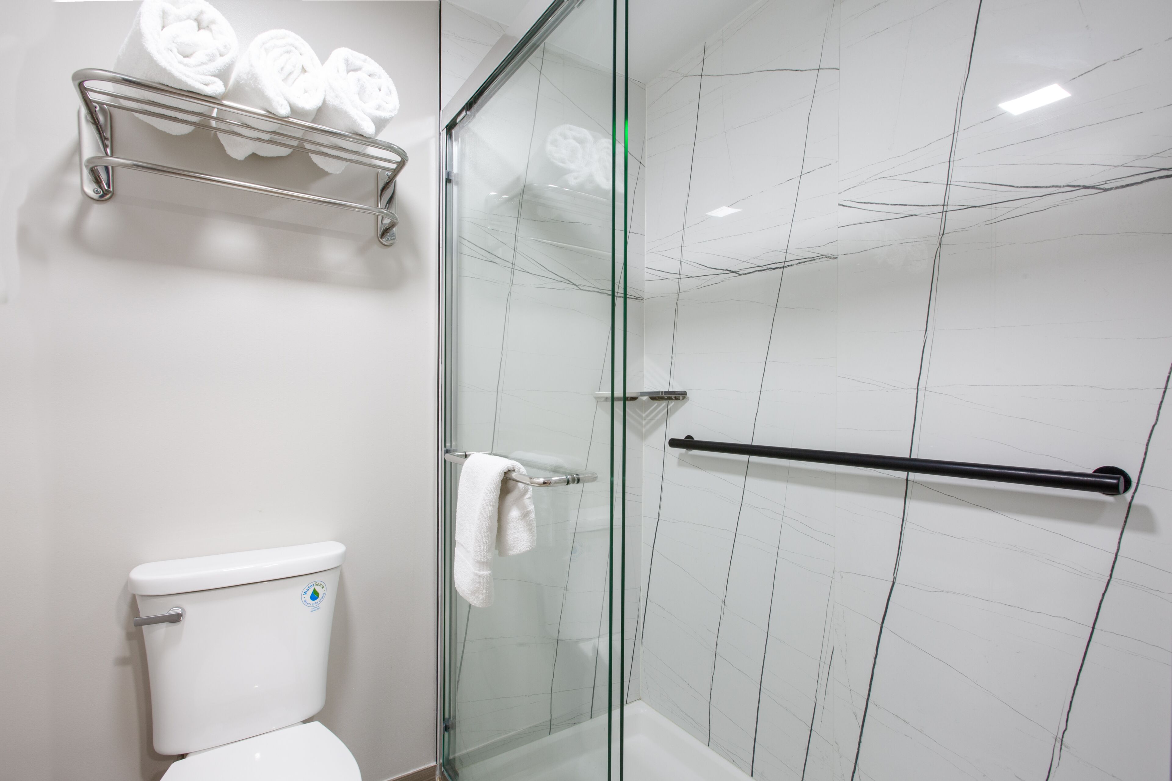 A modern bathroom with a glass shower enclosure, a toilet, and a towel rack with rolled towels.