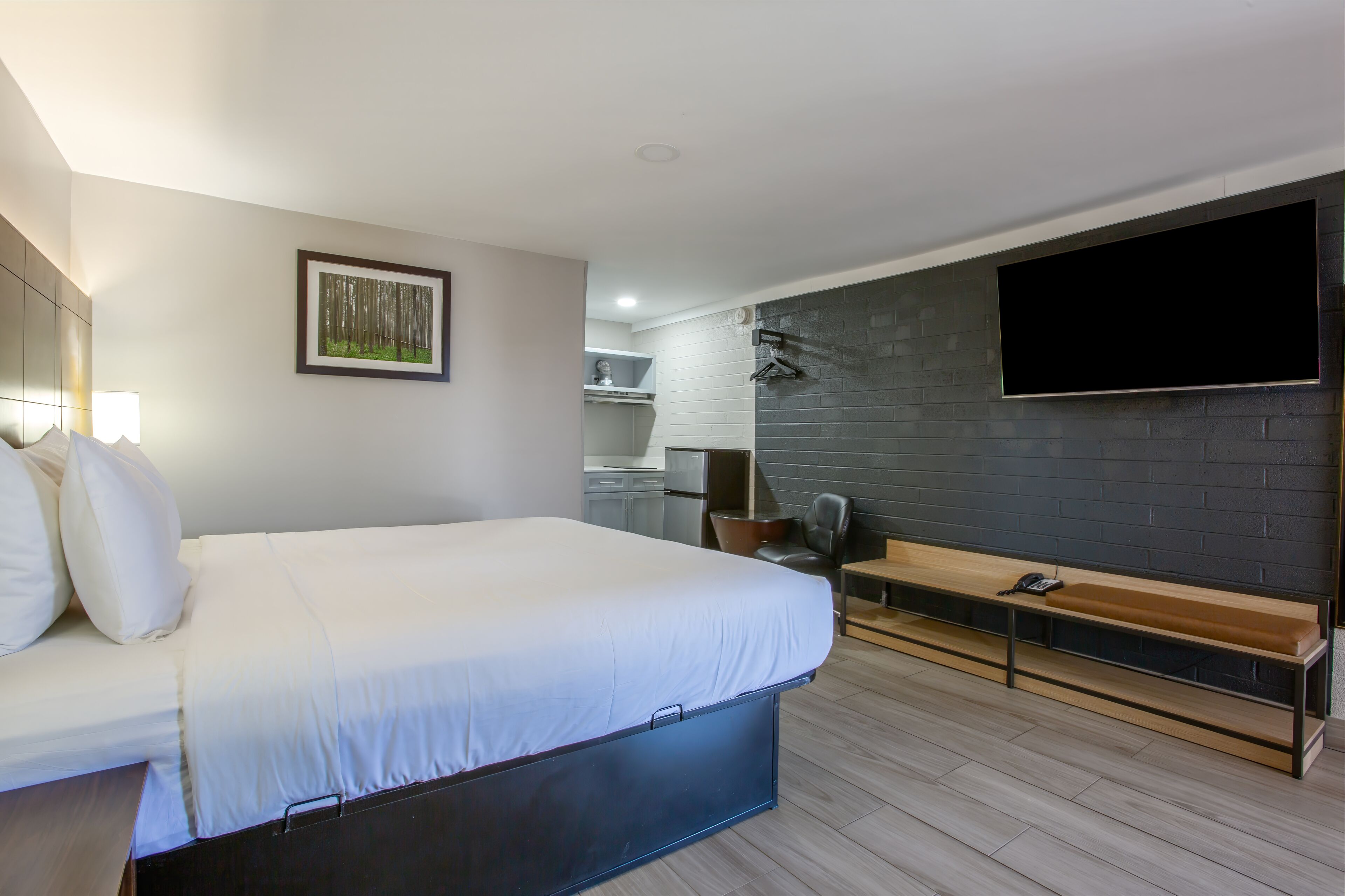 A modern hotel room with a bed, a bench, a flat-screen TV, and a painting on the wall.