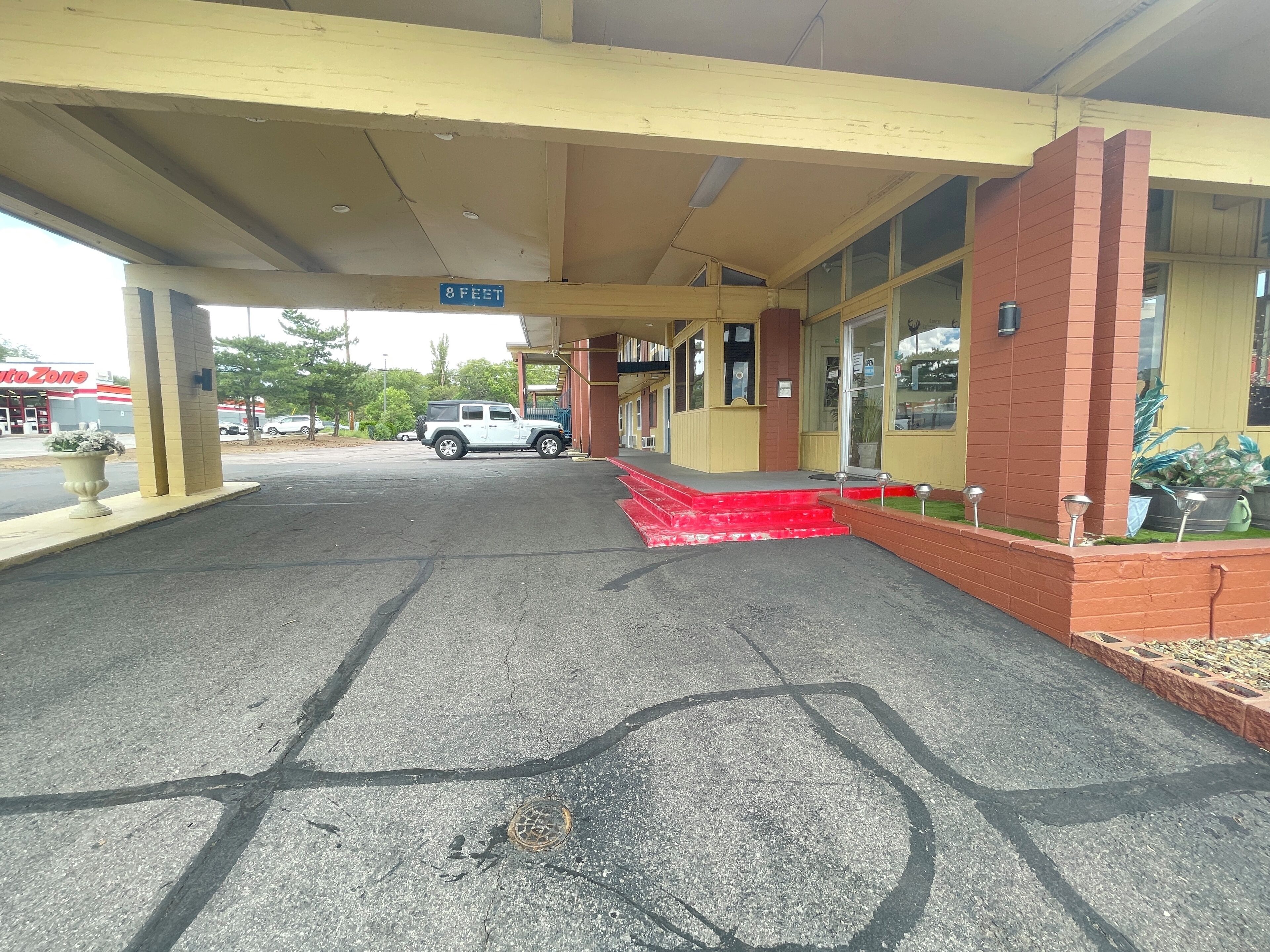 A parking area with a white SUV, a building with a yellow and red facade, and a sign indicating '8 FEET'.