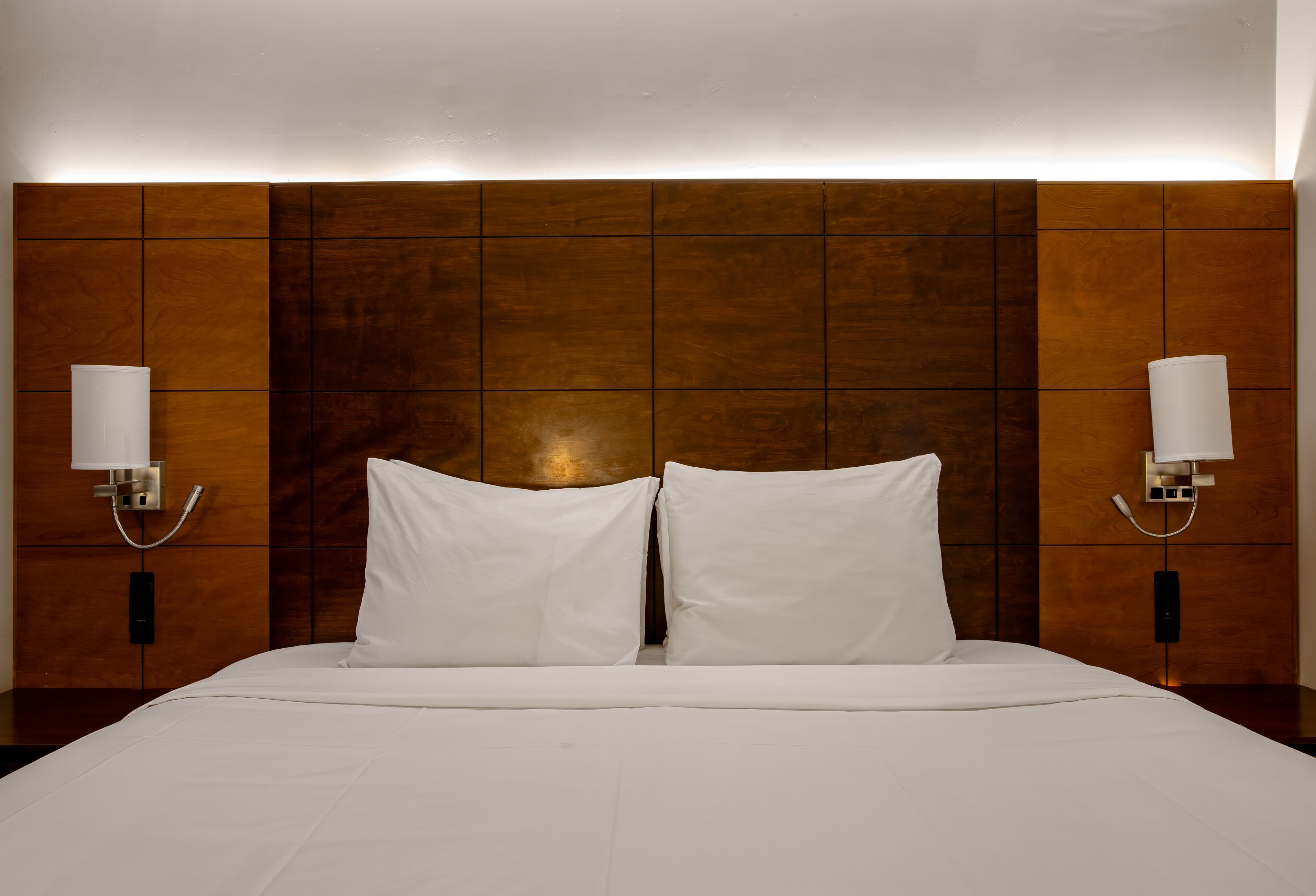 Una habitación de hotel con una cama grande, dos lámparas de noche y un cabecero de madera.