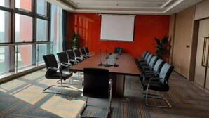 A conference room with a long table, multiple chairs, a projector, and a white screen. - Boutique Guodu Hotel (Nantong)