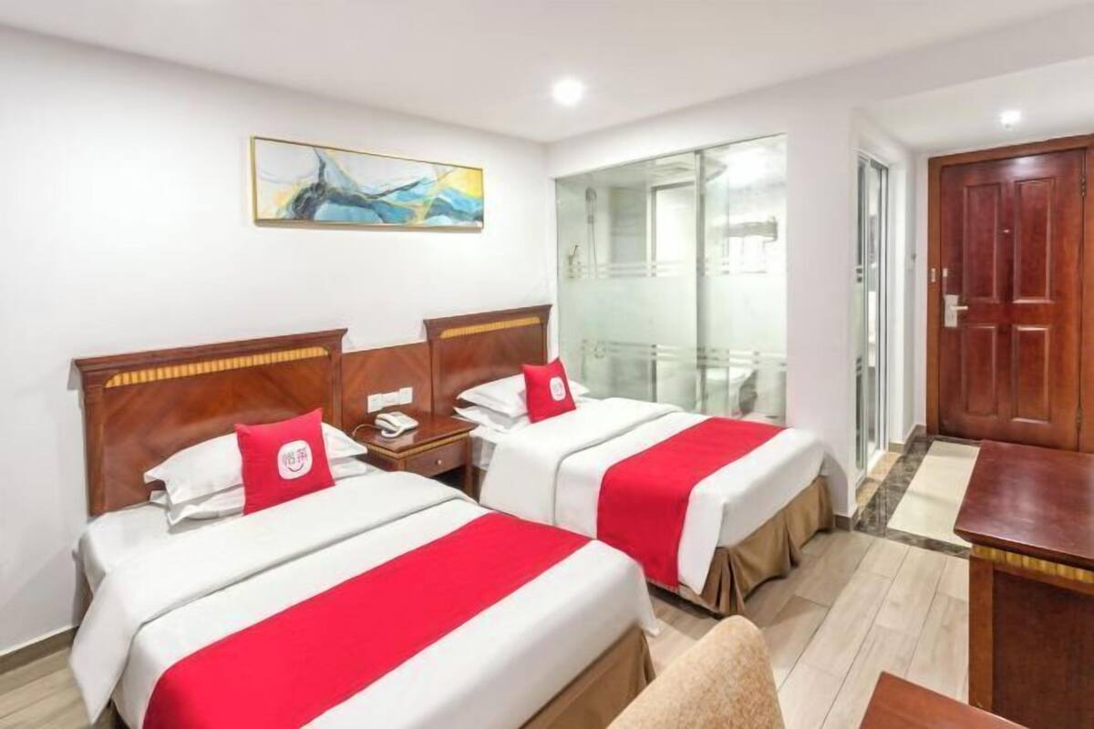 Hotelkamer met twee bedden, een houten hoofdbord, een nachtkastje met een telefoon, een rode kussen en een schilderij aan de muur, plus een schuifdeur naar een balkon.