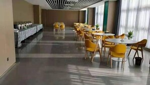 A spacious hotel dining area with yellow chairs and tables, a buffet line on the left, and large windows providing natural light. - Boutique Guodu Hotel (Nantong)