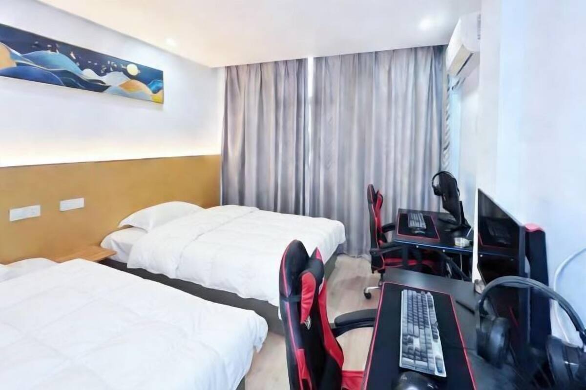 Een hotelkamer met twee bedden, een bureau met een computer en een koptelefoon, en een schilderij aan de muur.