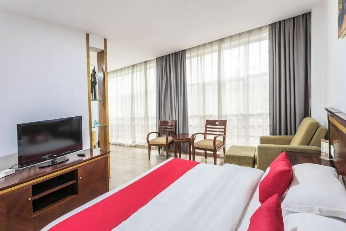Een hotelkamer met een bed, een televisie op een houten standaard, een bureau en een stoel.