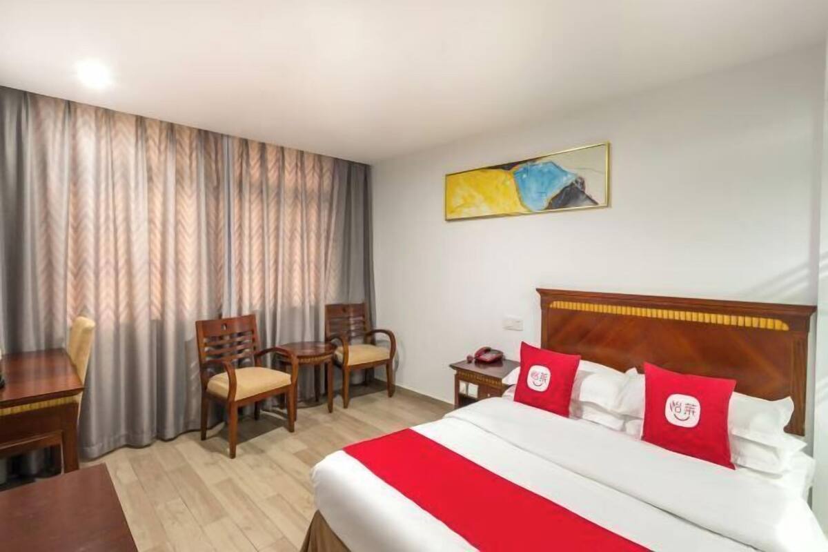 Een hotelkamer met een bed, twee stoelen, een klein tafeltje en een schilderij aan de muur.