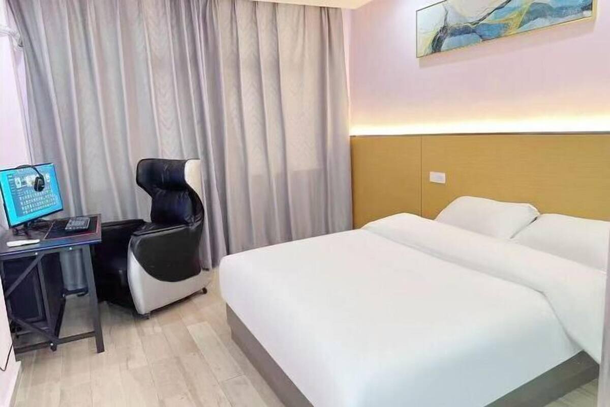 Een hotelkamer met een bed, een bureau met een computer, een stoel en een gordijn.
