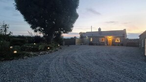 Une allée de gravier mène à une maison en pierre dont l'entrée est illuminée.