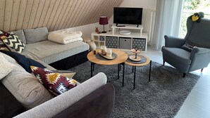 Una sala de estar moderna con techo inclinado, un sofá, una silla, un televisor y una pequeña mesa con objetos decorativos.