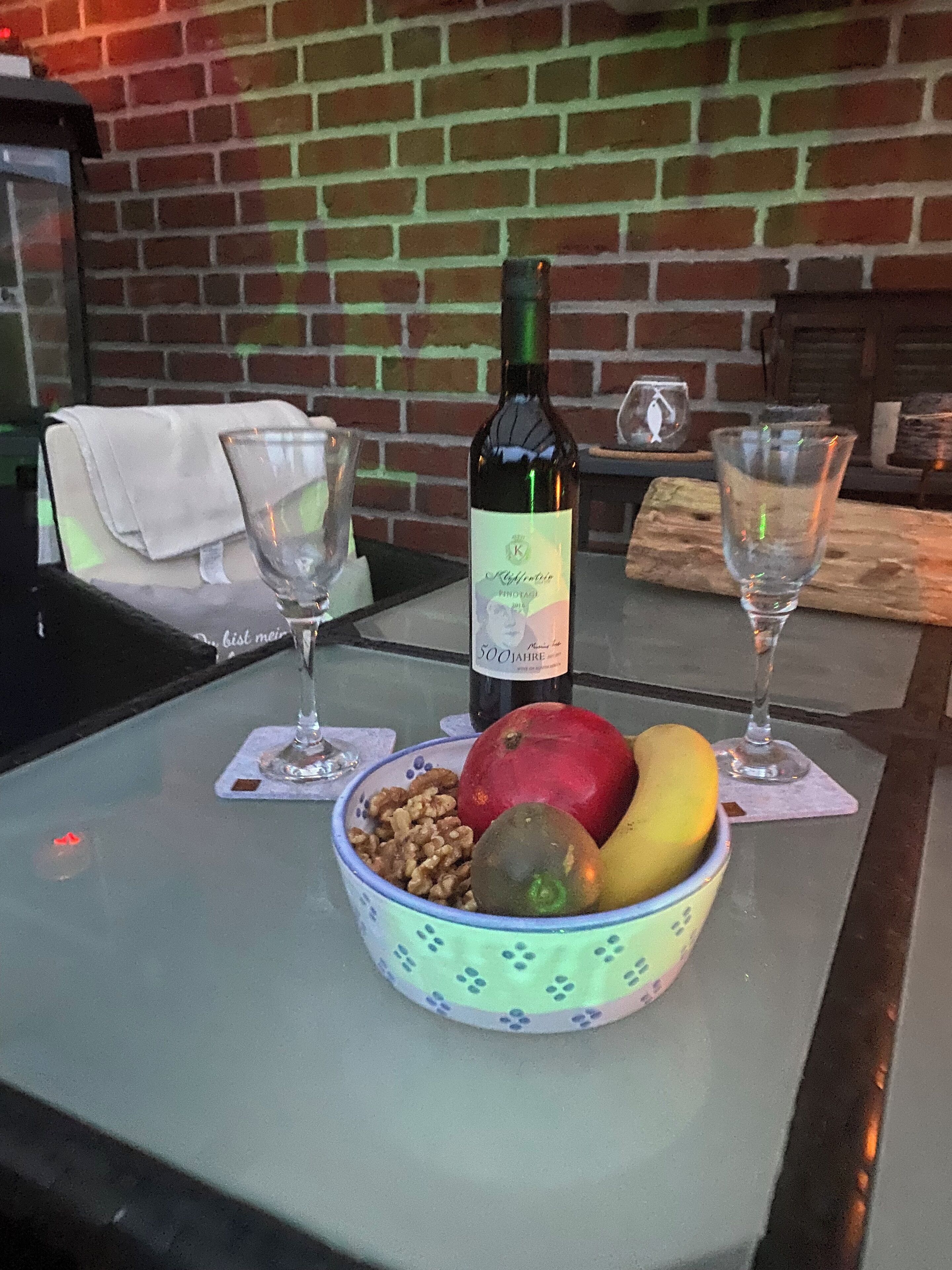 A table with a bottle of wine, two glasses, and a bowl of fruit.