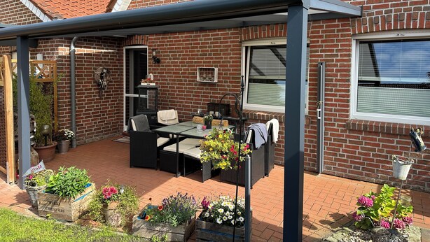 Un patio con mobiliario cubierto, una casa de ladrillo y plantas en macetas.