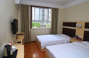Une chambre d’hôtel avec deux lits, une télévision, un bureau avec une bouilloire et une fenêtre avec des rideaux.