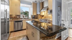 A modern kitchen with stainless steel appliances, beige cabinetry, and a large island with a black granite countertop.