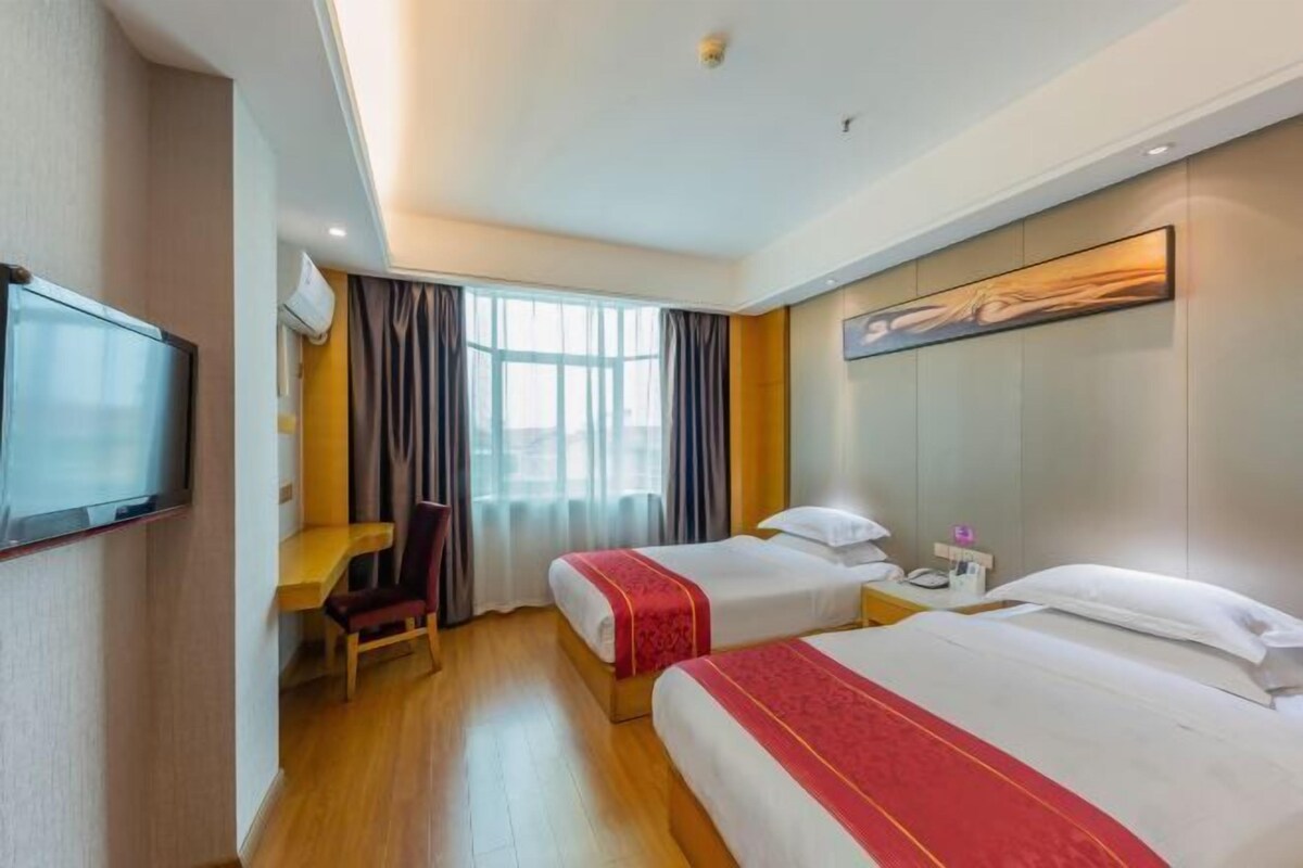 Habitación de hotel con dos camas, un escritorio, una silla, un televisor y un cuadro en la pared.