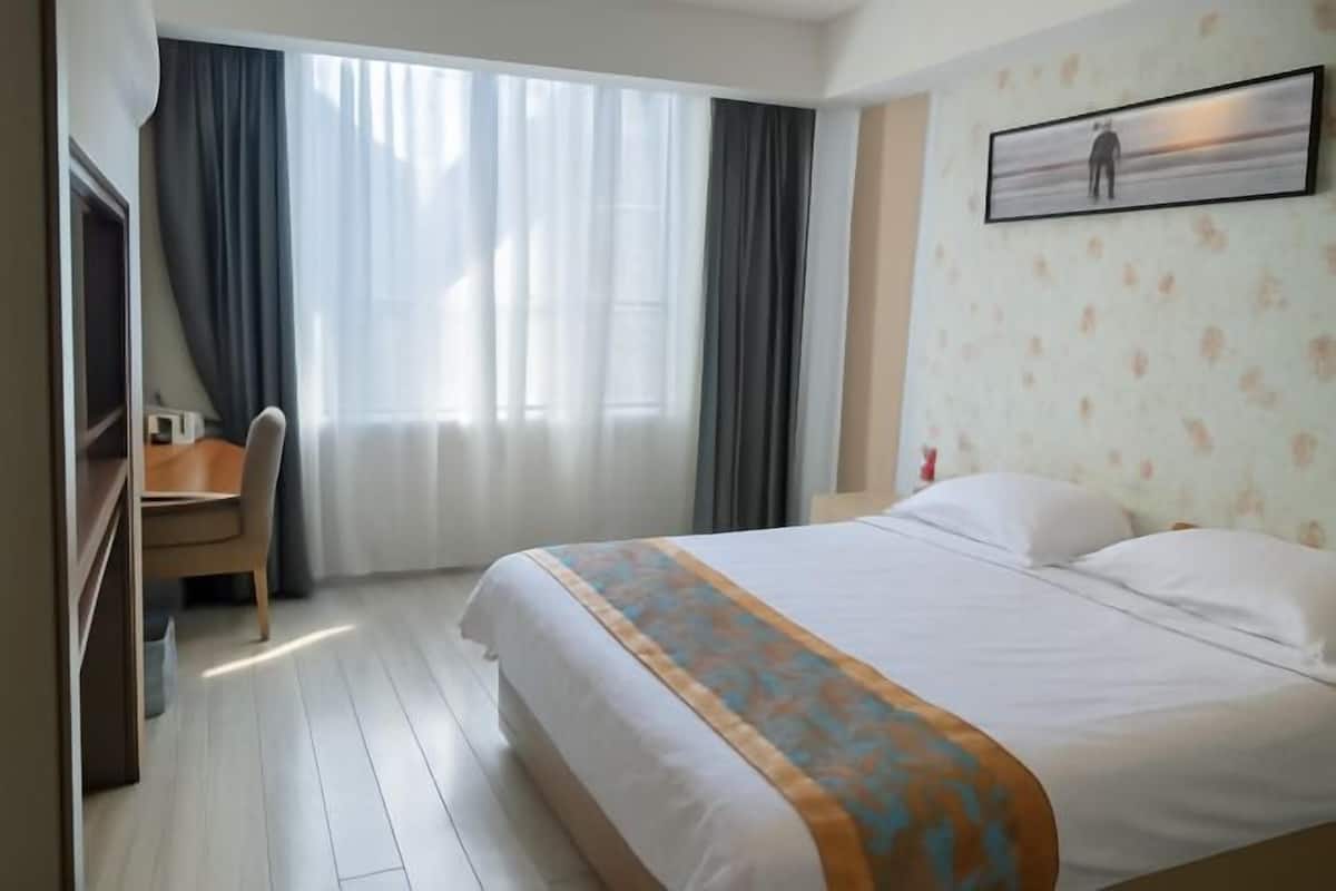 A hotel room with a bed, a desk, a chair, a TV, and a window with curtains.