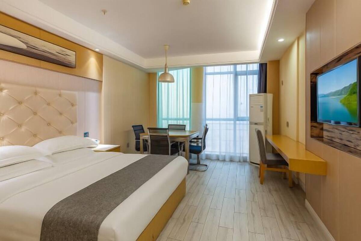 A hotel room with a large bed, a desk, a chair, a television, and a window with curtains.