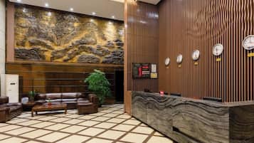 A hotel lobby with a reception desk, seating area, and a large decorative wall.