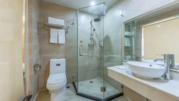 A modern bathroom with a glass-enclosed shower, a white toilet, and a sink with a mirror above it.
