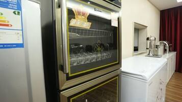 A kitchen with a built-in oven and microwave, a refrigerator, and a window with curtains.