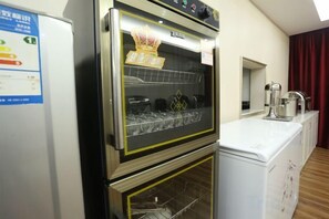 A kitchen with a built-in oven and microwave, a refrigerator, and a window with curtains.