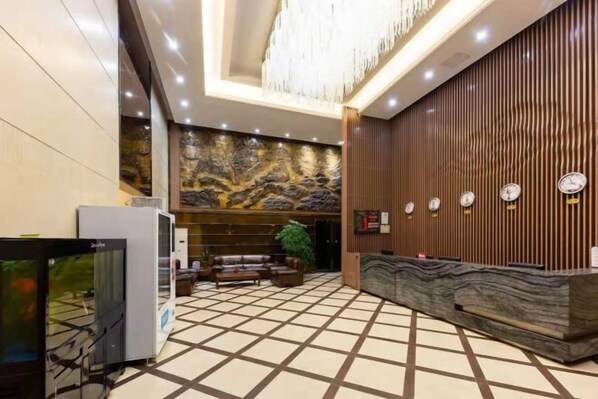A lobby with a reception desk, a large chandelier, a stone wall, and a clock on the wall. - Tianhai Yuyuan Hotel (Jiujiang Railway Station) (Jiujiang)