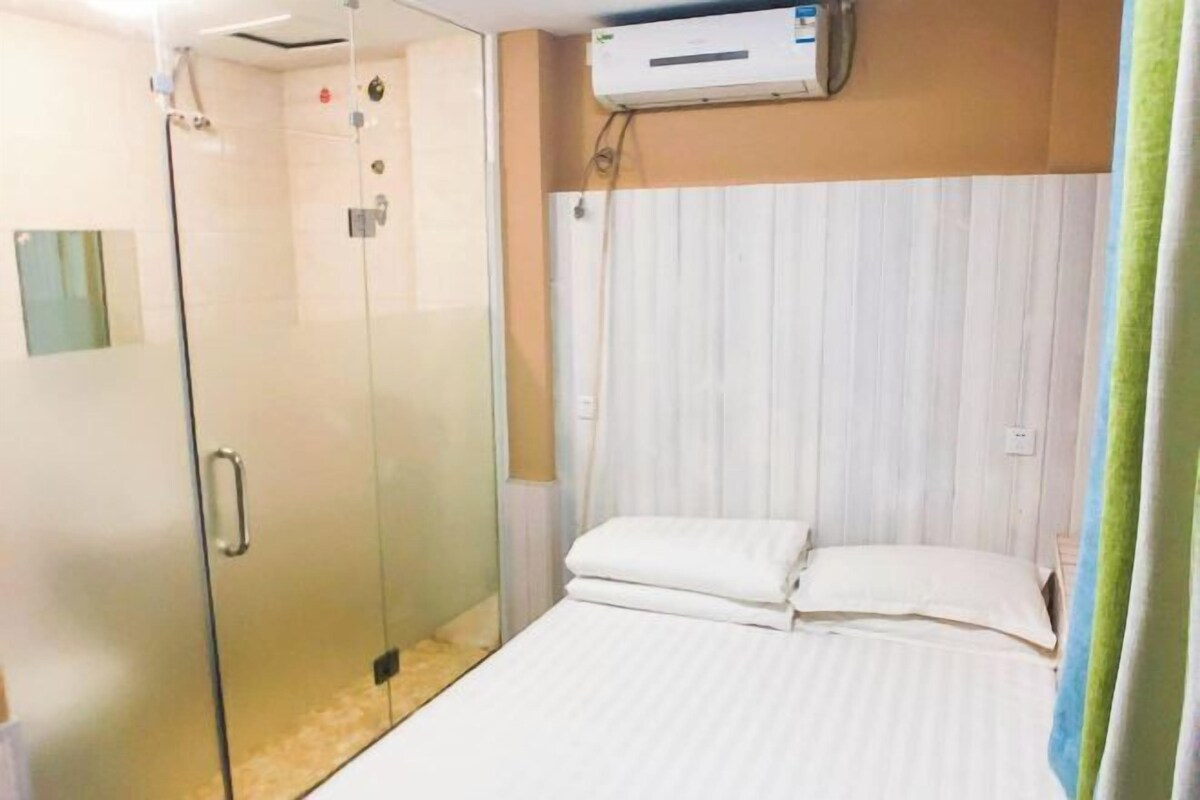 Habitación de hotel con ducha de vidrio, cama con ropa de cama blanca y aire acondicionado de pared.