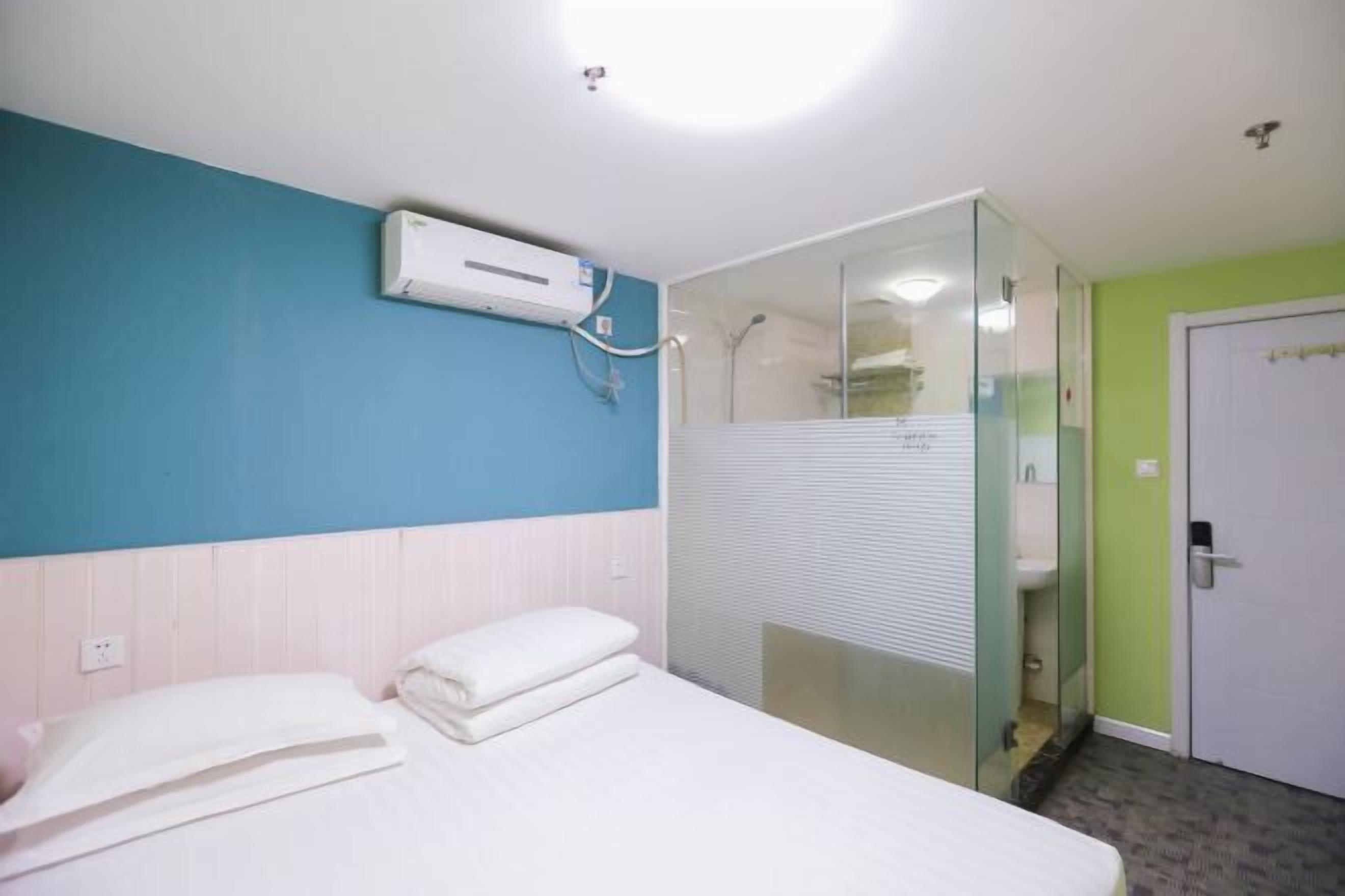 Quarto de hotel com cama, box de vidro, porta branca e ar condicionado na parede.