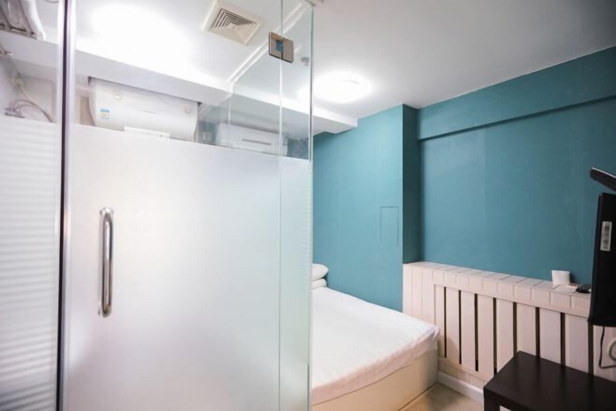 Une chambre avec une douche en verre, un lit blanc, un radiateur blanc et un mur de couleur turquoise.