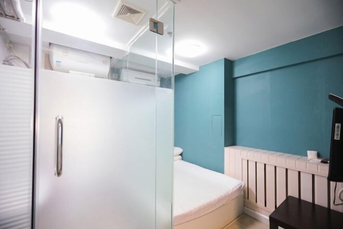 Un dormitorio con cabina de ducha de vidrio, una cama blanca, un radiador blanco y una mesa negra.