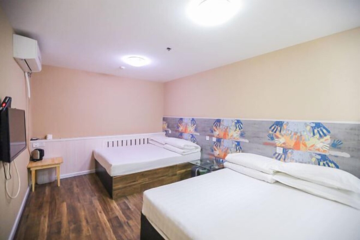 Une chambre d’hôtel avec deux lits, une petite table, un radiateur fixé au mur et une fresque murale abstraite aux couleurs vives.