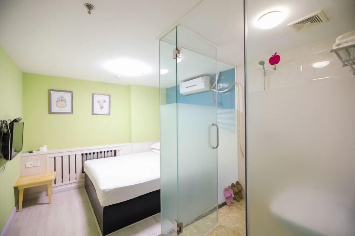 Habitación de hotel moderna con cabina de ducha de vidrio, cama, mesita de noche pequeña y calentador de pared.