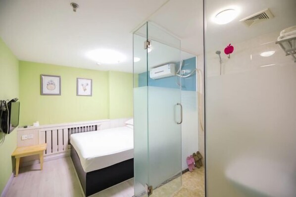 Habitación de hotel moderna con cabina de ducha de vidrio, cama, mesita de noche pequeña y calentador de pared.