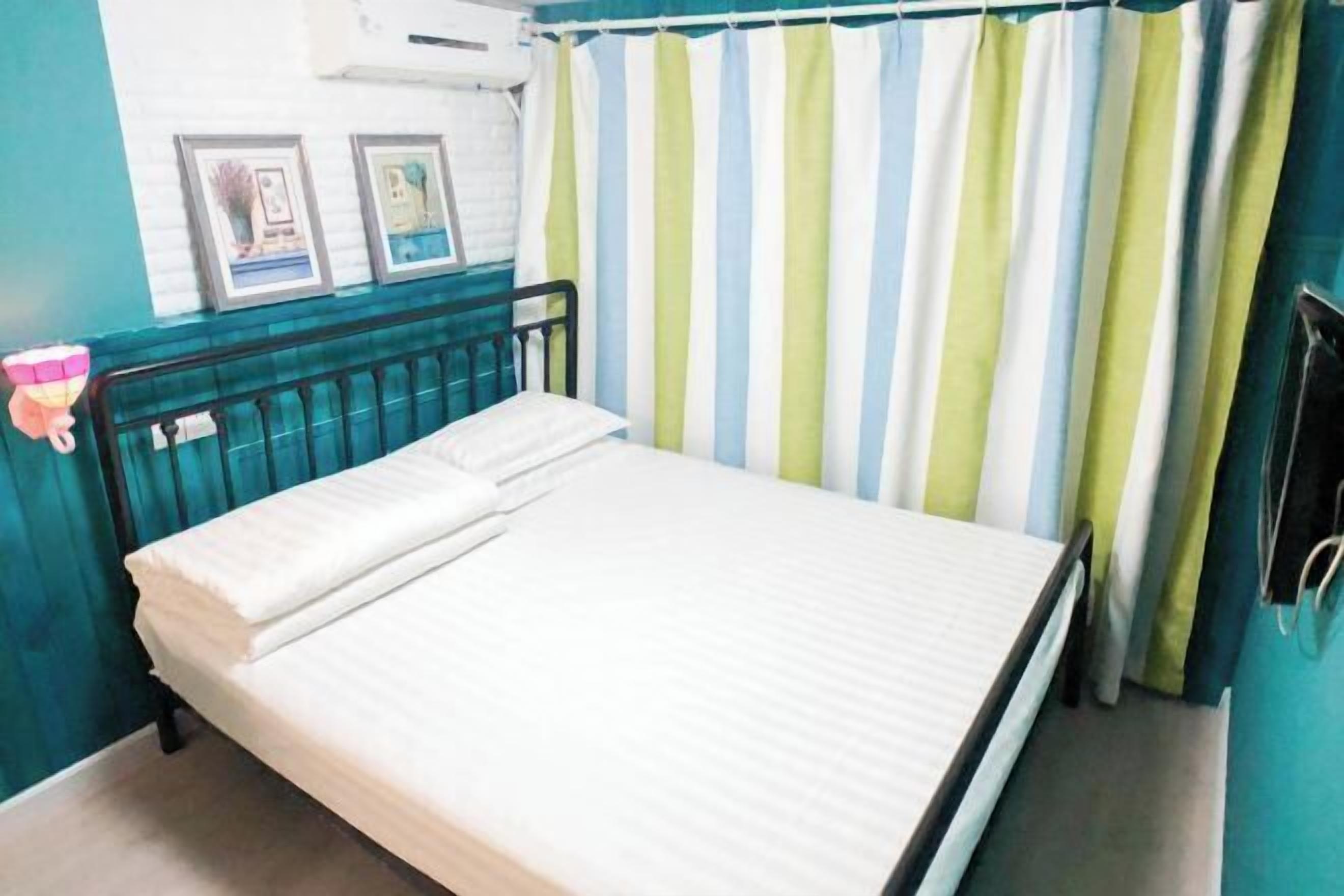 Un lit simple avec un matelas et des oreillers blancs, une tête de lit en métal noir et un rideau à rayures.