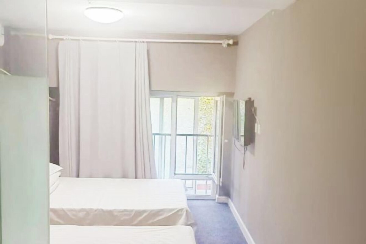 A bedroom with two beds, a window with curtains, and a door.
