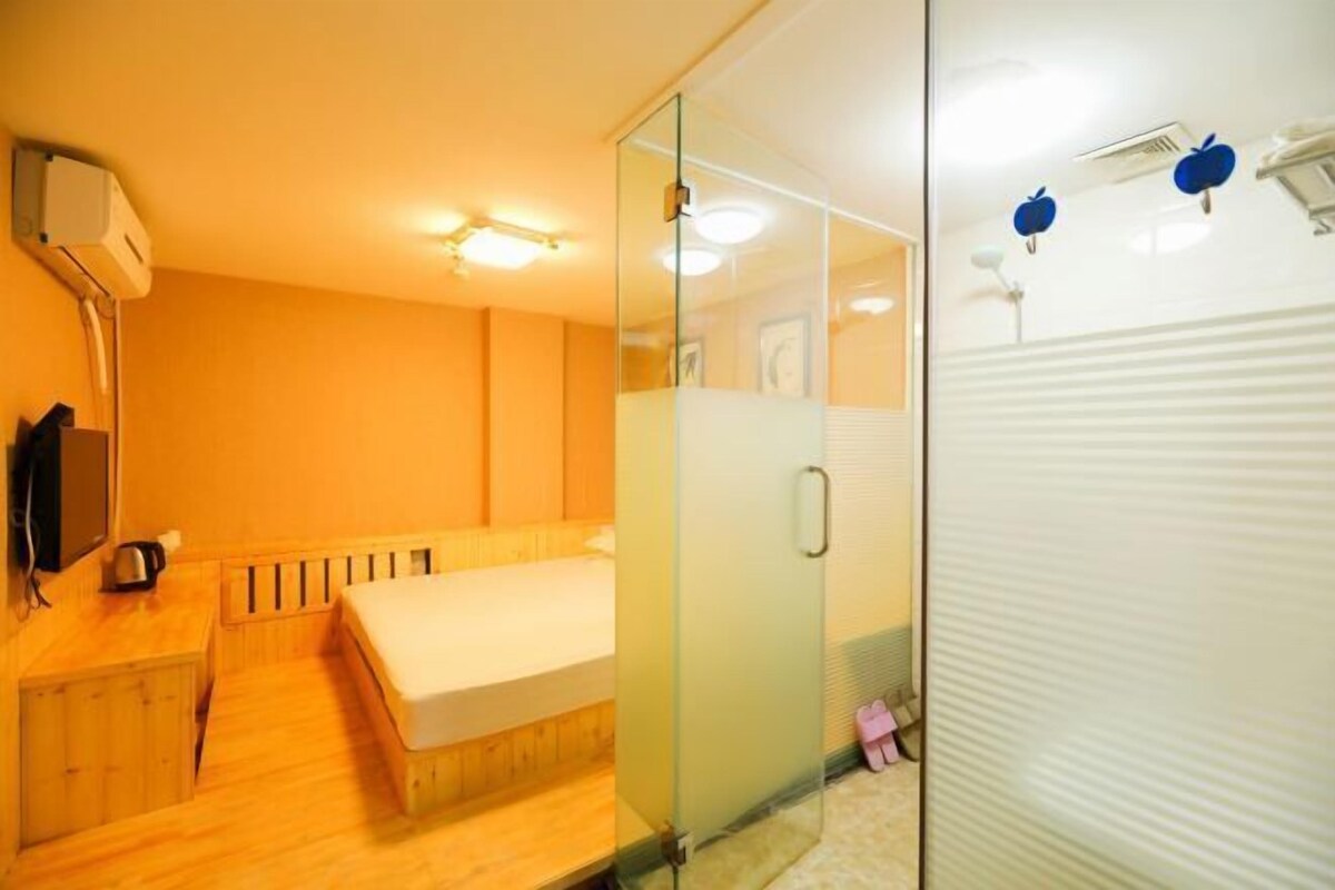 Una habitación de hotel moderna con un escritorio de madera, una cama, un separador de vidrio y un radiador blanco.