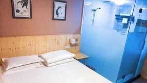 A hotel room with a wooden headboard, a bed with white linens, a small bedside table with a lamp, and a glass shower enclosure. - Ruida Business Hotel Shenyang (Shenyang)