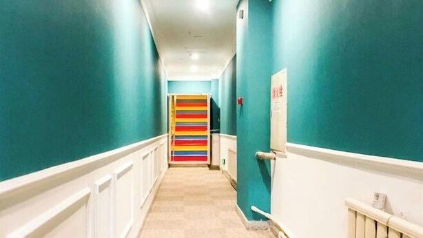 A hallway with teal walls, white trim, and a colorful striped door at the end. - Ruida Business Hotel Shenyang (Shenyang)