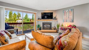 A living room with a fireplace, a television, and a large window overlooking a deck. - Mountain Dream in Adorable Frisco - 5 Ski Resorts and Lake Dillon (Frisco)