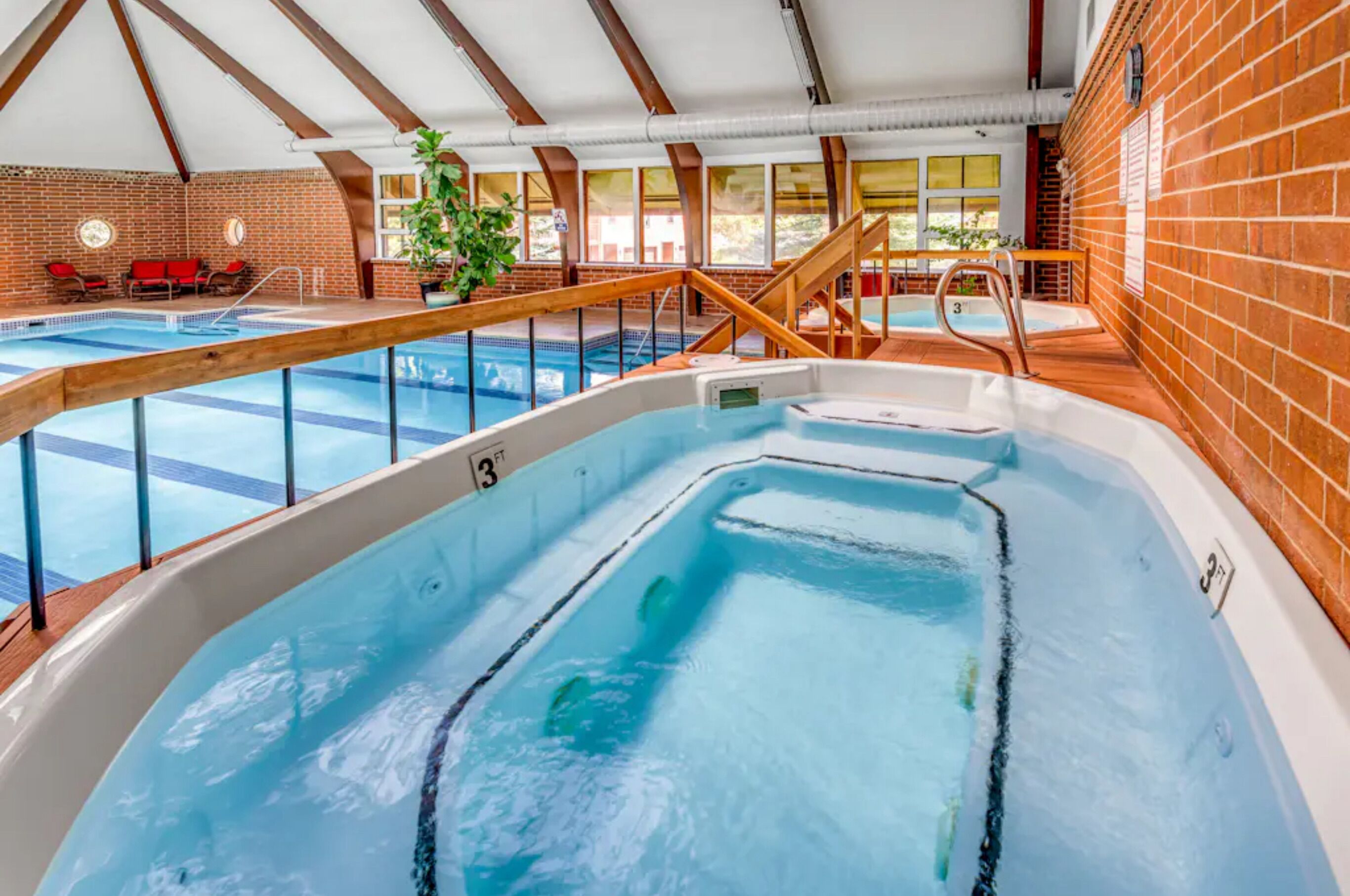 Une piscine intérieure dotée d’un jacuzzi, d’une terrasse en bois et de murs en briques.