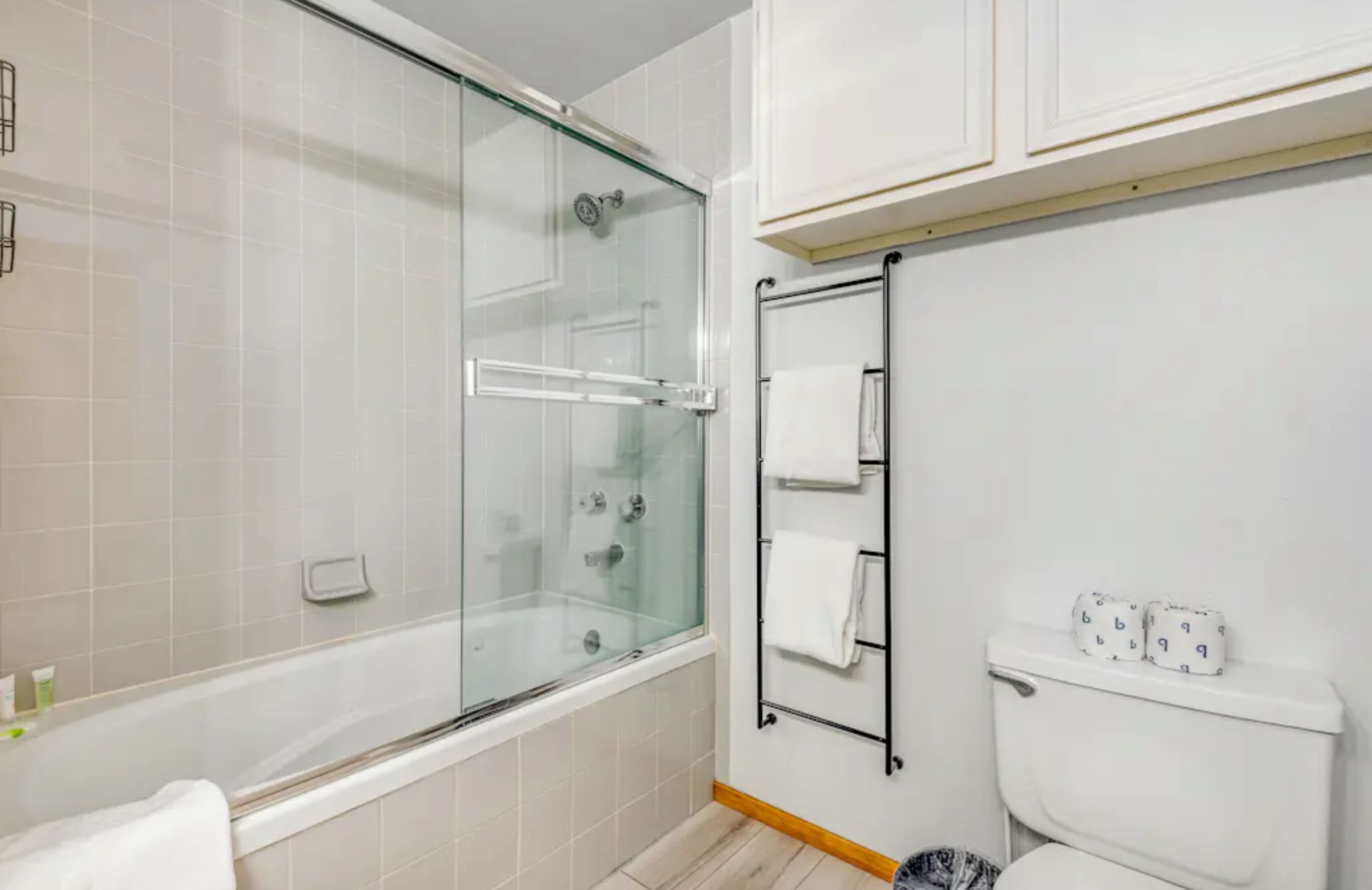 Ein modernes Badezimmer mit einer gläsernen Duschkabine, einer Badewanne, einem WC mit Handtuchhalter und einer Toilettenpapierhalterung.