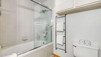 Ein modernes Badezimmer mit einer gläsernen Duschkabine, einer Badewanne, einem WC mit Handtuchhalter und einer Toilettenpapierhalterung.