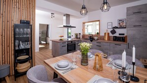A modern kitchen with a wooden dining table set for four, a built-in oven, and a large window providing natural light. - Eggert Alm Apartments (Ilsenburg (Harz))