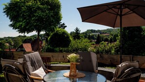 An outdoor seating area with a round table, chairs, and a large umbrella. - Eggert Alm Apartments (Ilsenburg (Harz))
